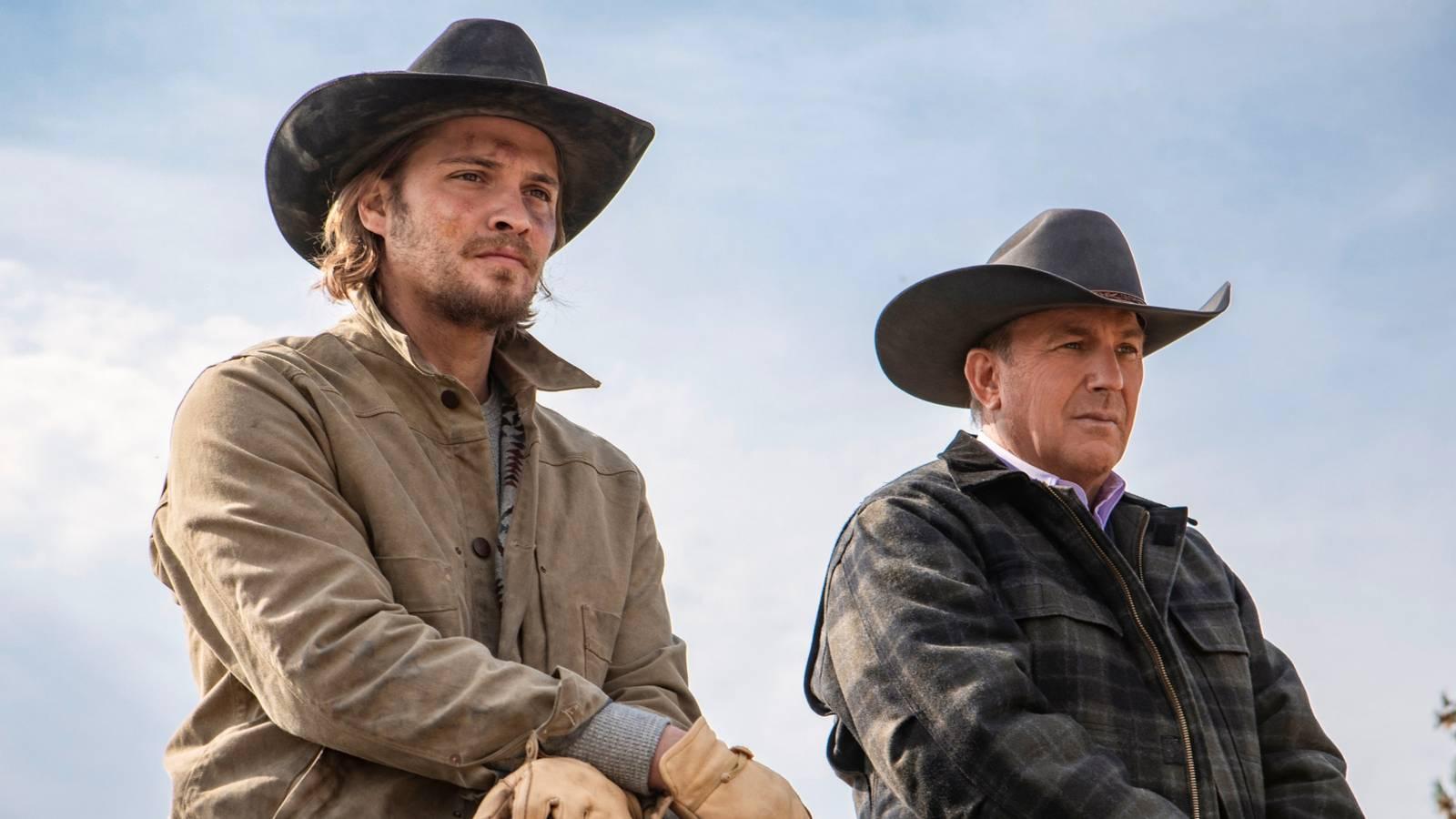 Luke Grimes e Kevin Costner em vestimenta ocidental observando o horizonte em Yellowstone.