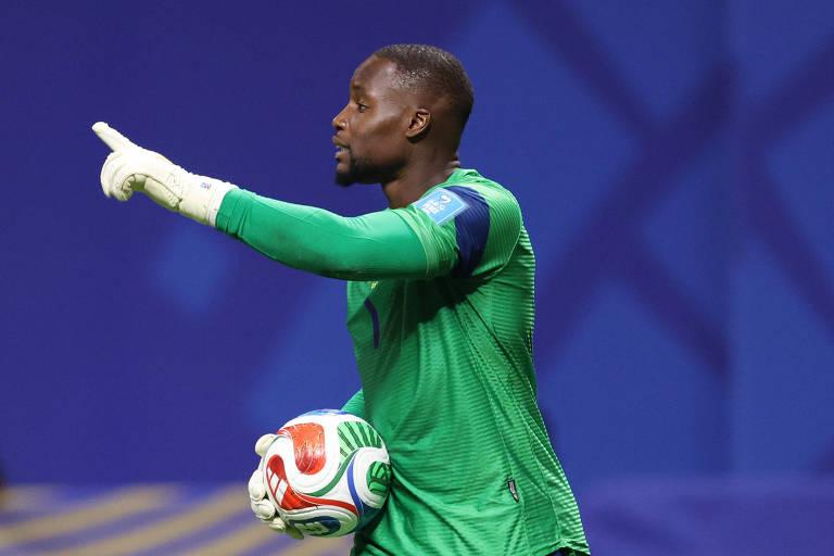 Goleiro vestido com uniforme verde e luvas brancas segura bola de futebol com as duas mãos.