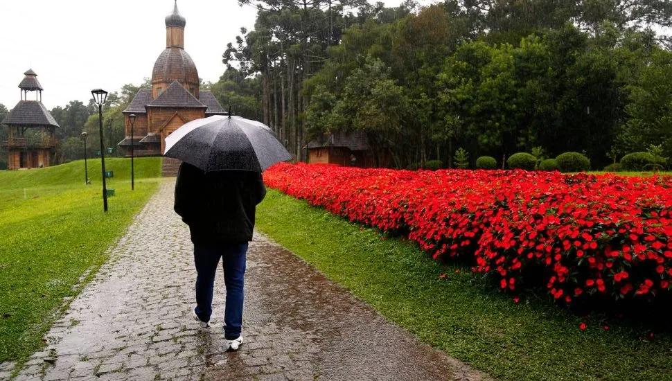 Imagem mostra uma pessoa com um guarda-chuva em um parque.